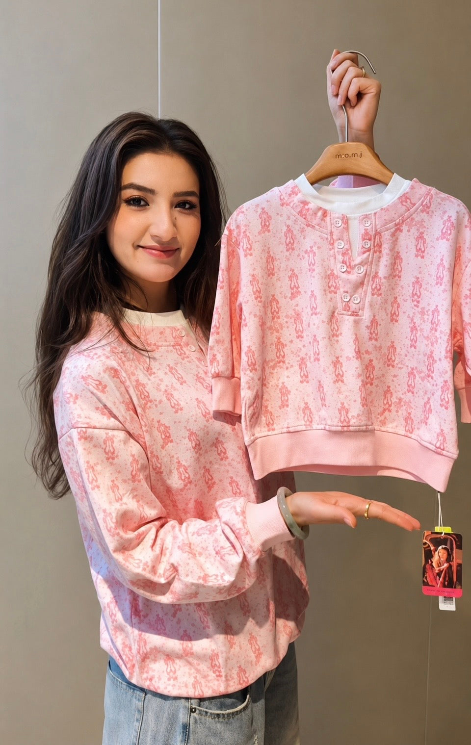 Woman presenting the pink ikat long-sleeve shirt on a hanger, showing its henley neckline and pattern.