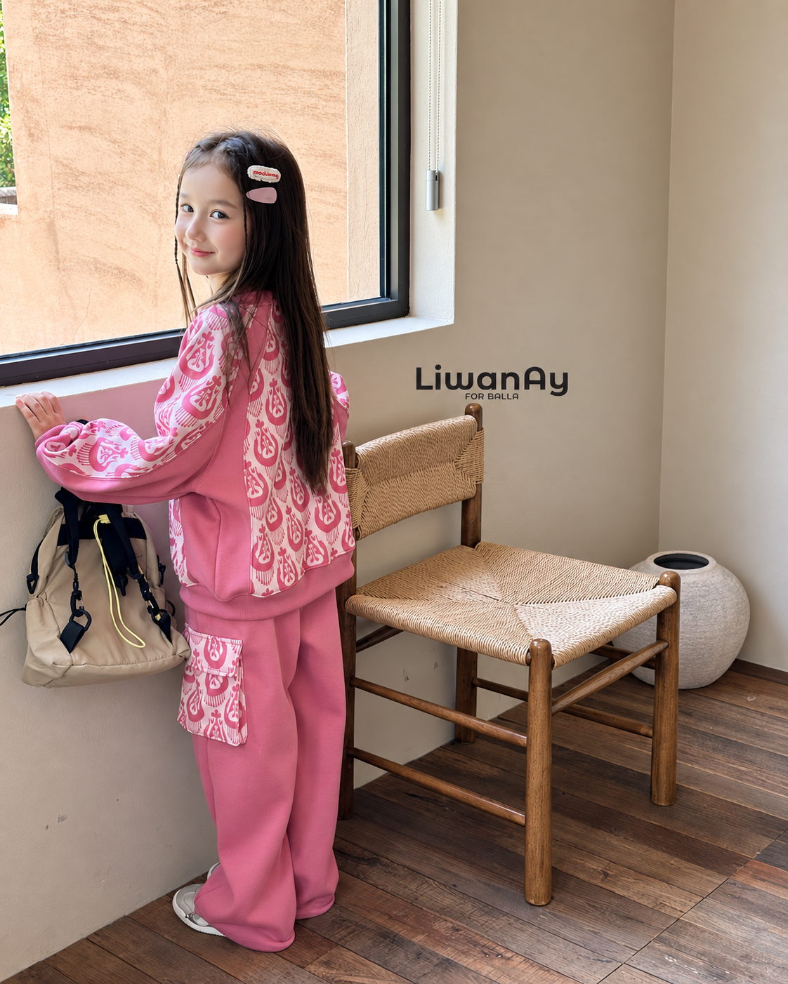 Back view of the girl in the pink ikat sweatshirt and cargo pants near a rattan chair.