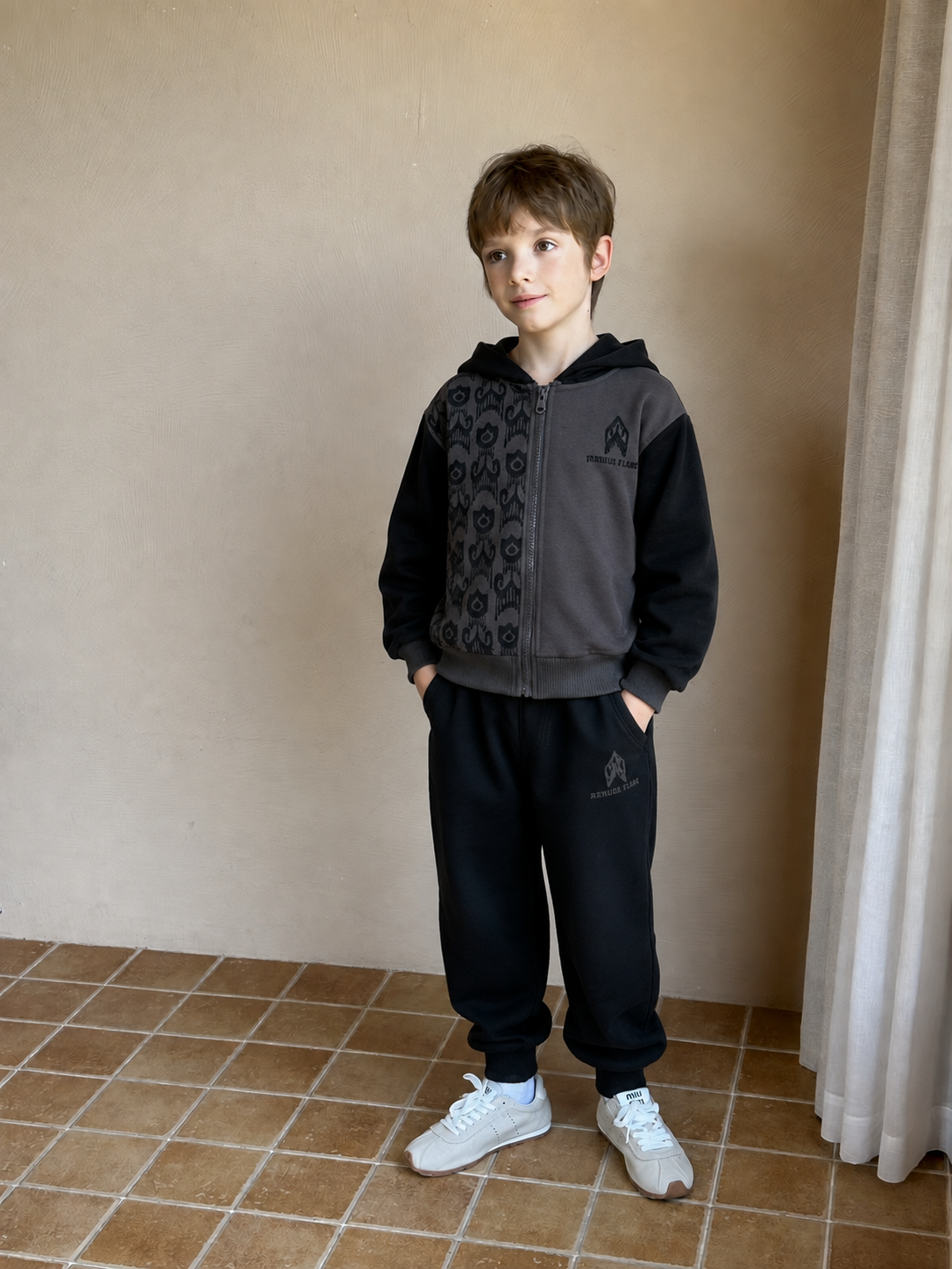 Boy wearing the charcoal ikat zip hoodie with patterned panel and black joggers, standing on a tiled patio