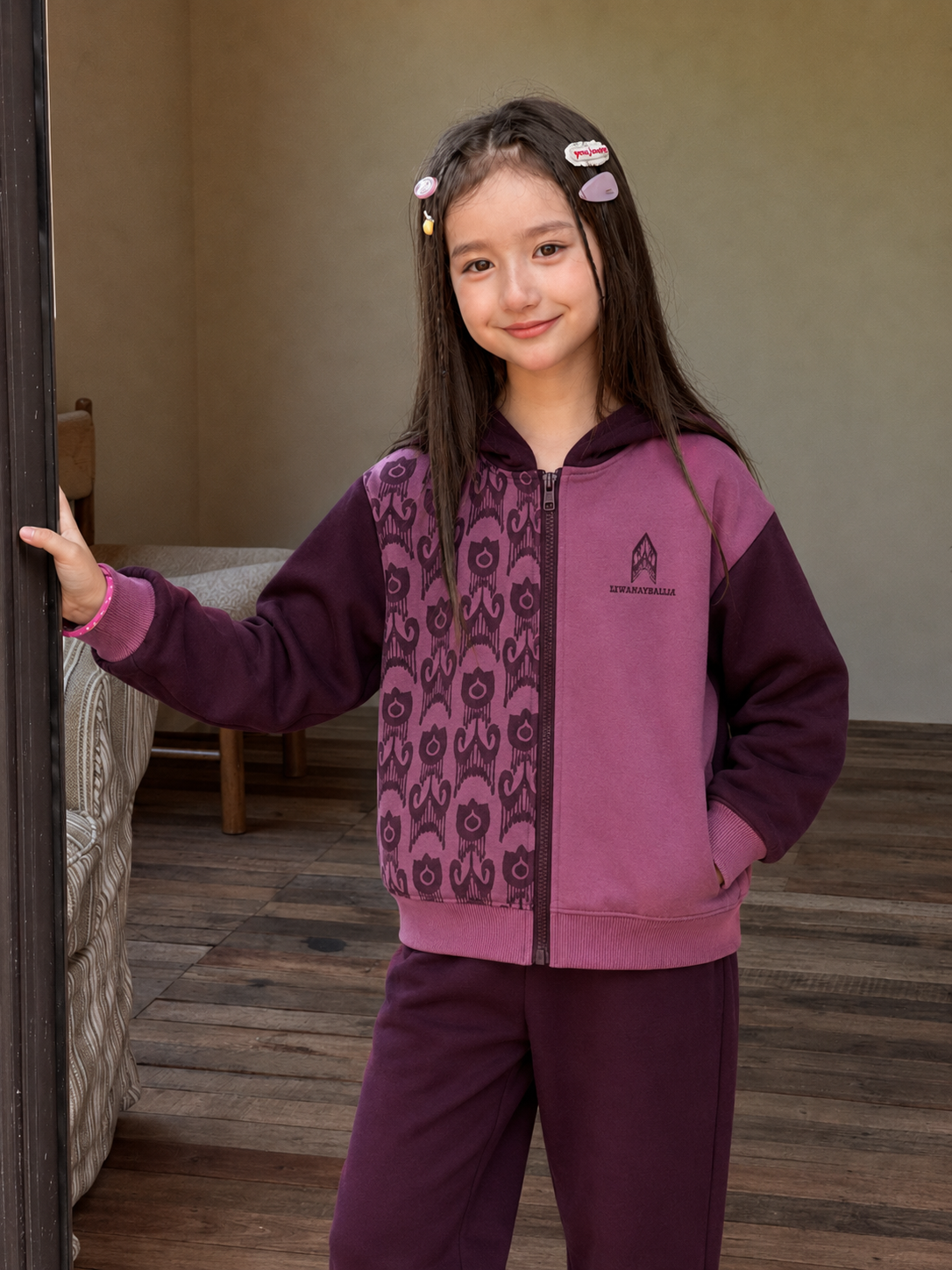 Girl wearing the purple zip-up hoodie with a dark atlas pattern panel and matching joggers, standing in a doorway