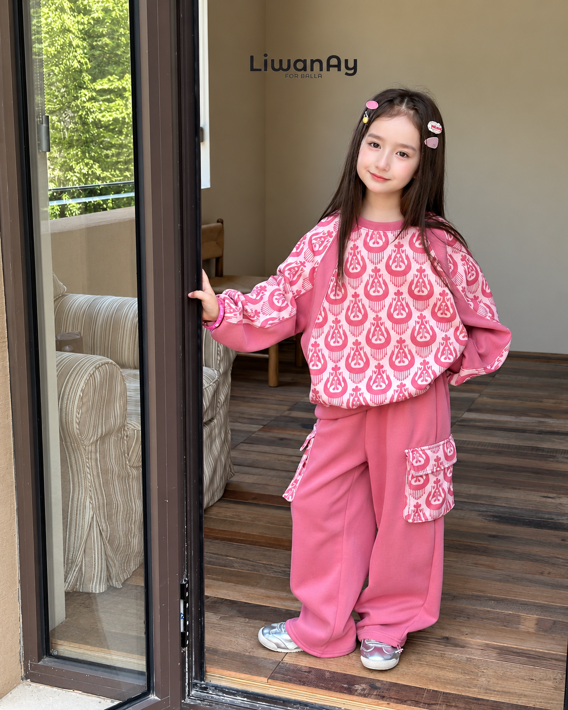 Girl standing in a doorway wearing a pink ikat sweatshirt and pink cargo pants with patterned pockets.