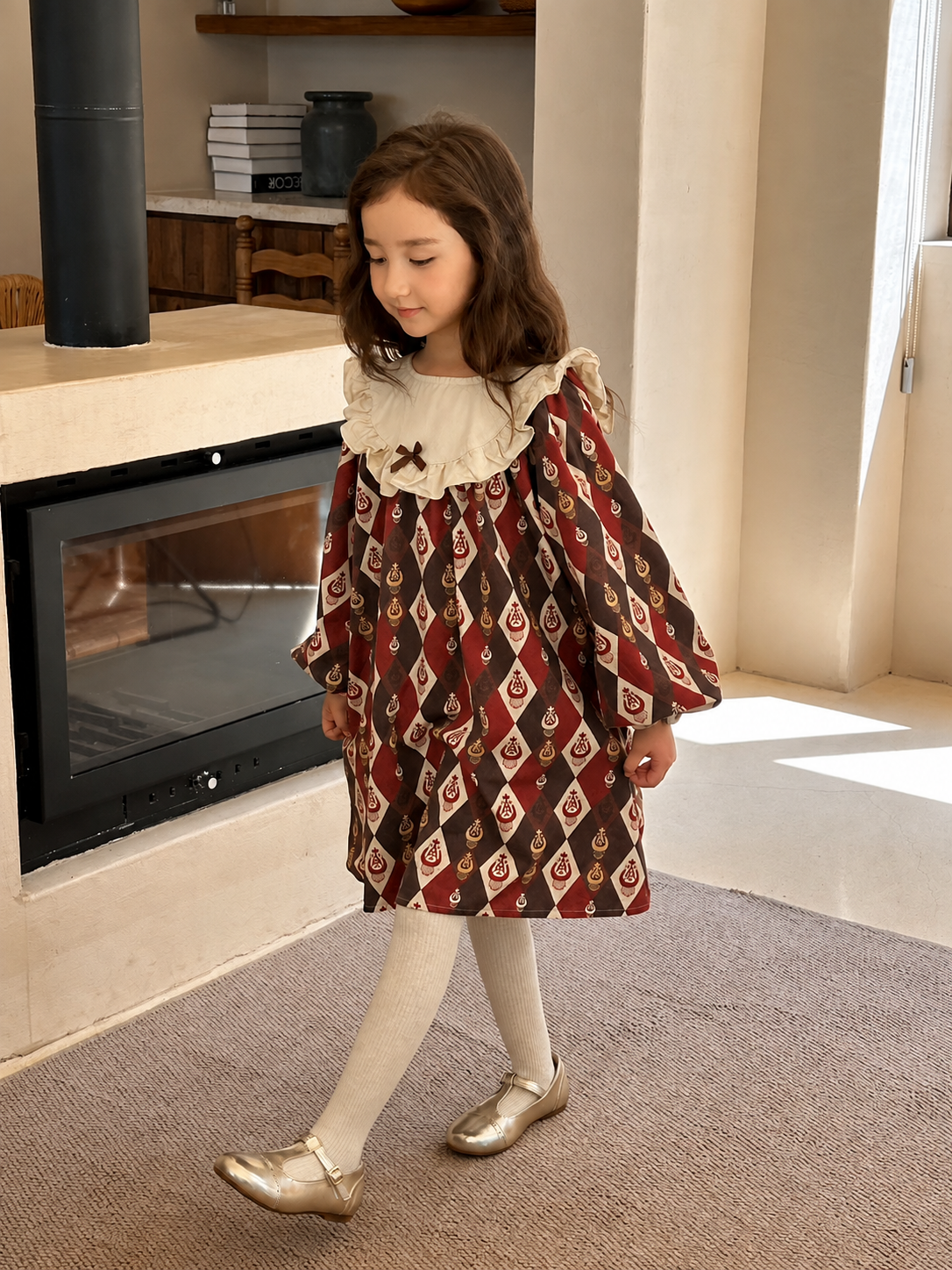 Girl walking past a modern fireplace in the burgundy diamond-ikat dress with cream collar and gold shoes.