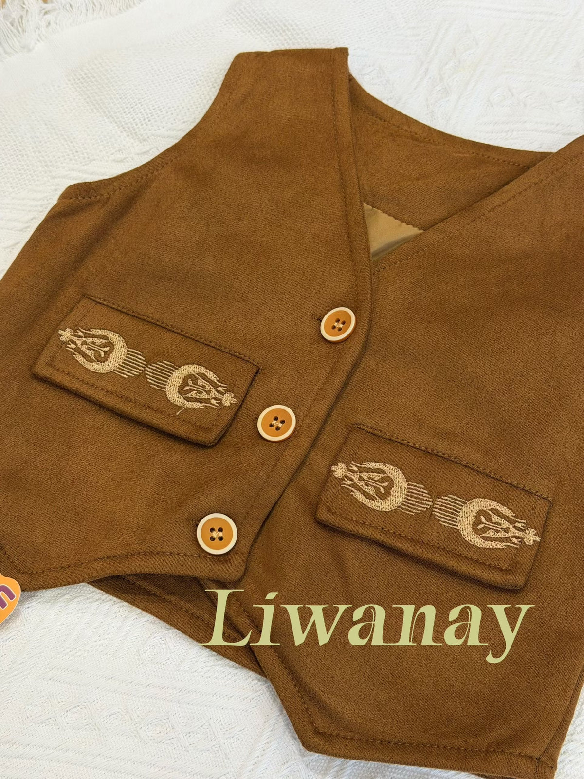 Close-up of the brown suede vest showing embroidered pockets and wooden button details on the front.