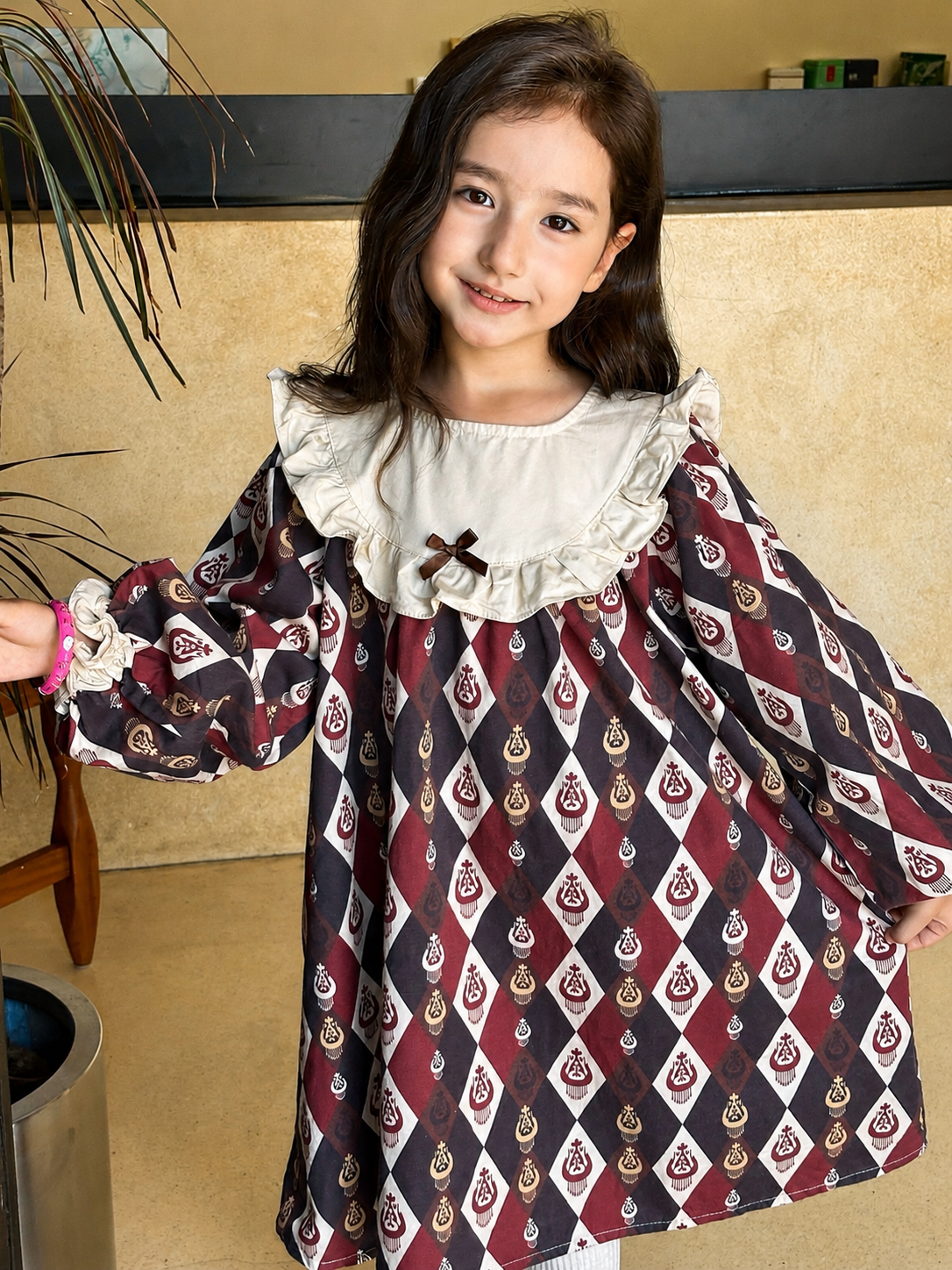Smiling girl with arms outstretched in the burgundy diamond-ikat dress with a cream ruffled collar.