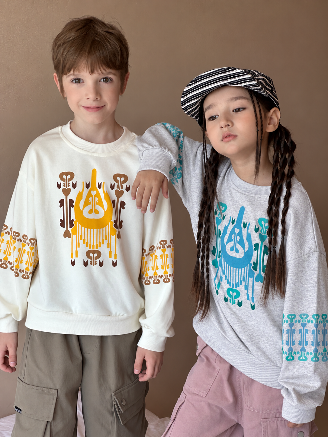 Boy and girl wearing the cotton atlas graphic sweatshirts in cream and grey with colorful patterned cuffs