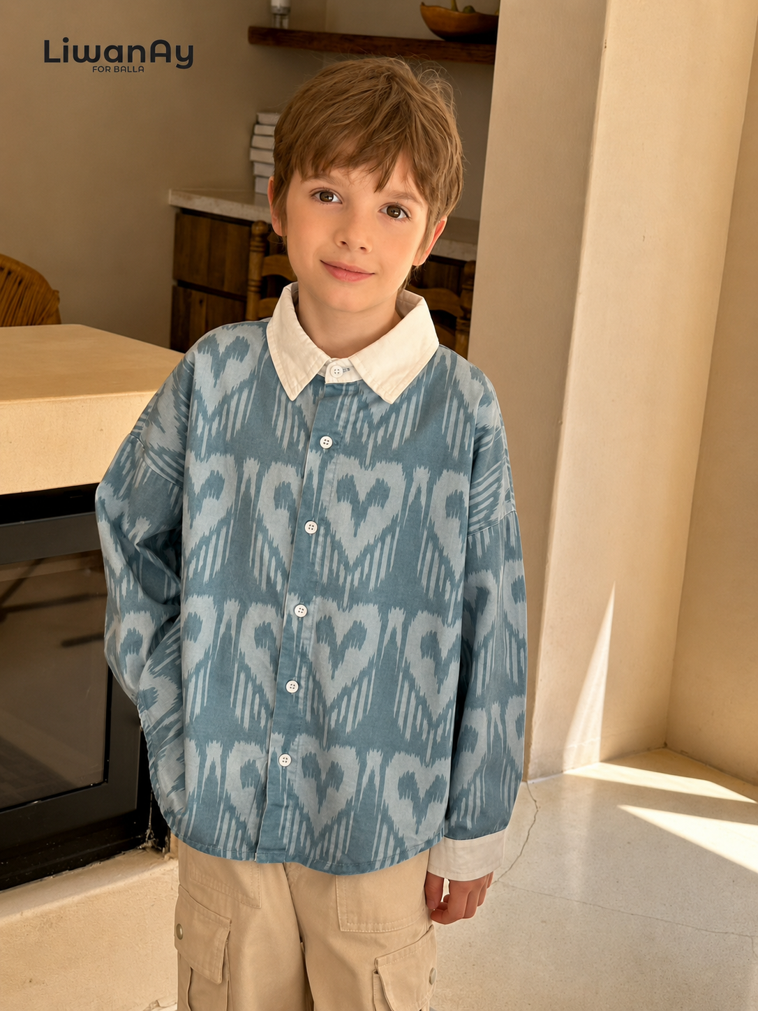 Boy wearing the blue ikat-pattern shirt with a white collar and beige cargo pants, posing in a home interior