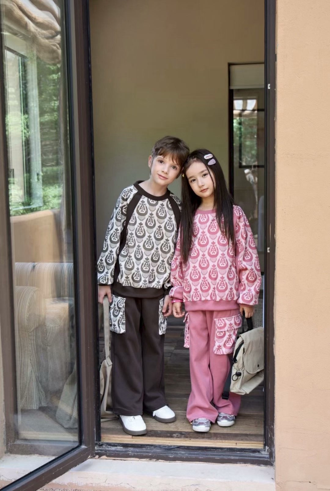 Two children standing in a doorway, wearing matching outfits with patterns.