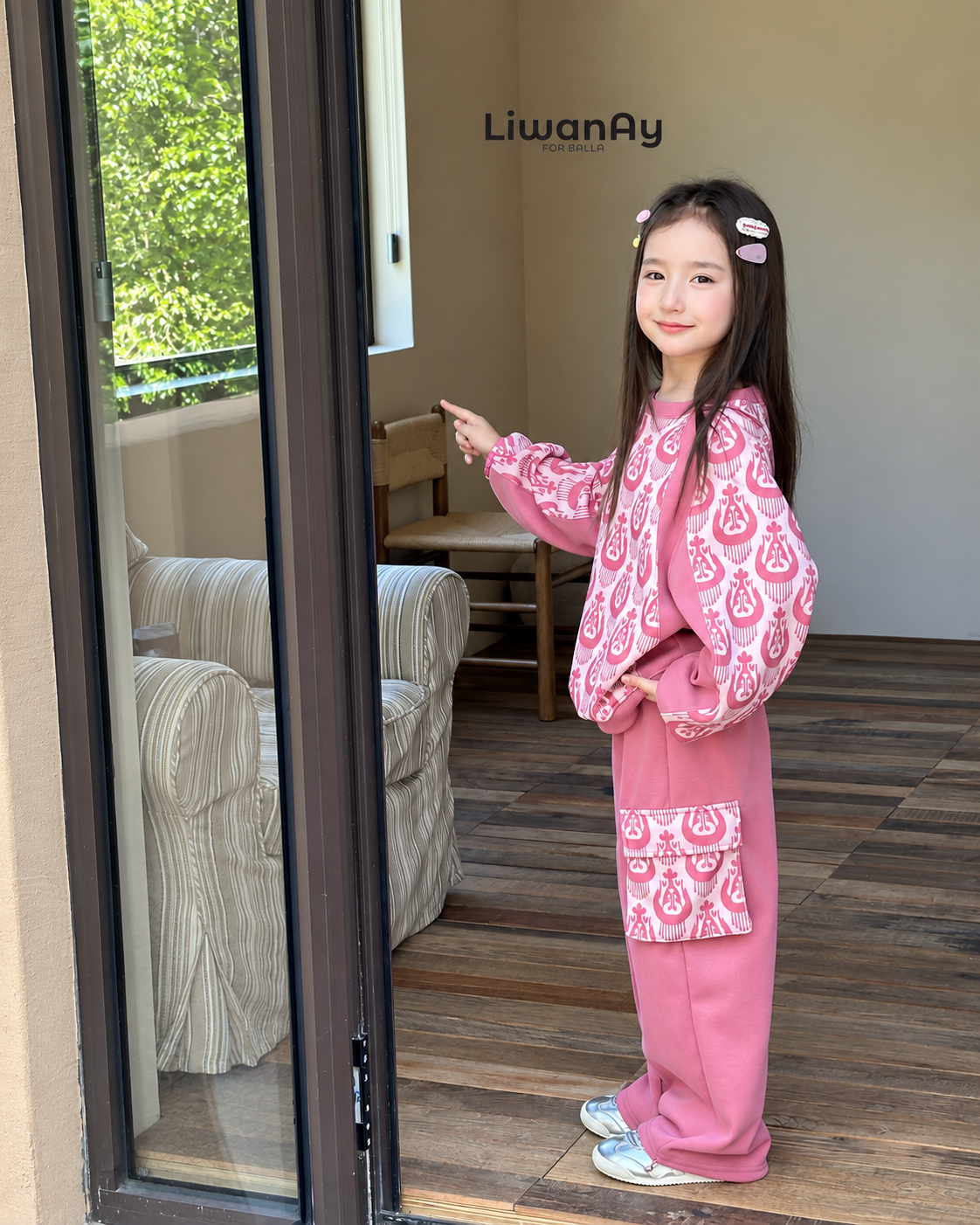 Girl standing in the doorway in the pink ikat sweatshirt set, hand on the door frame.