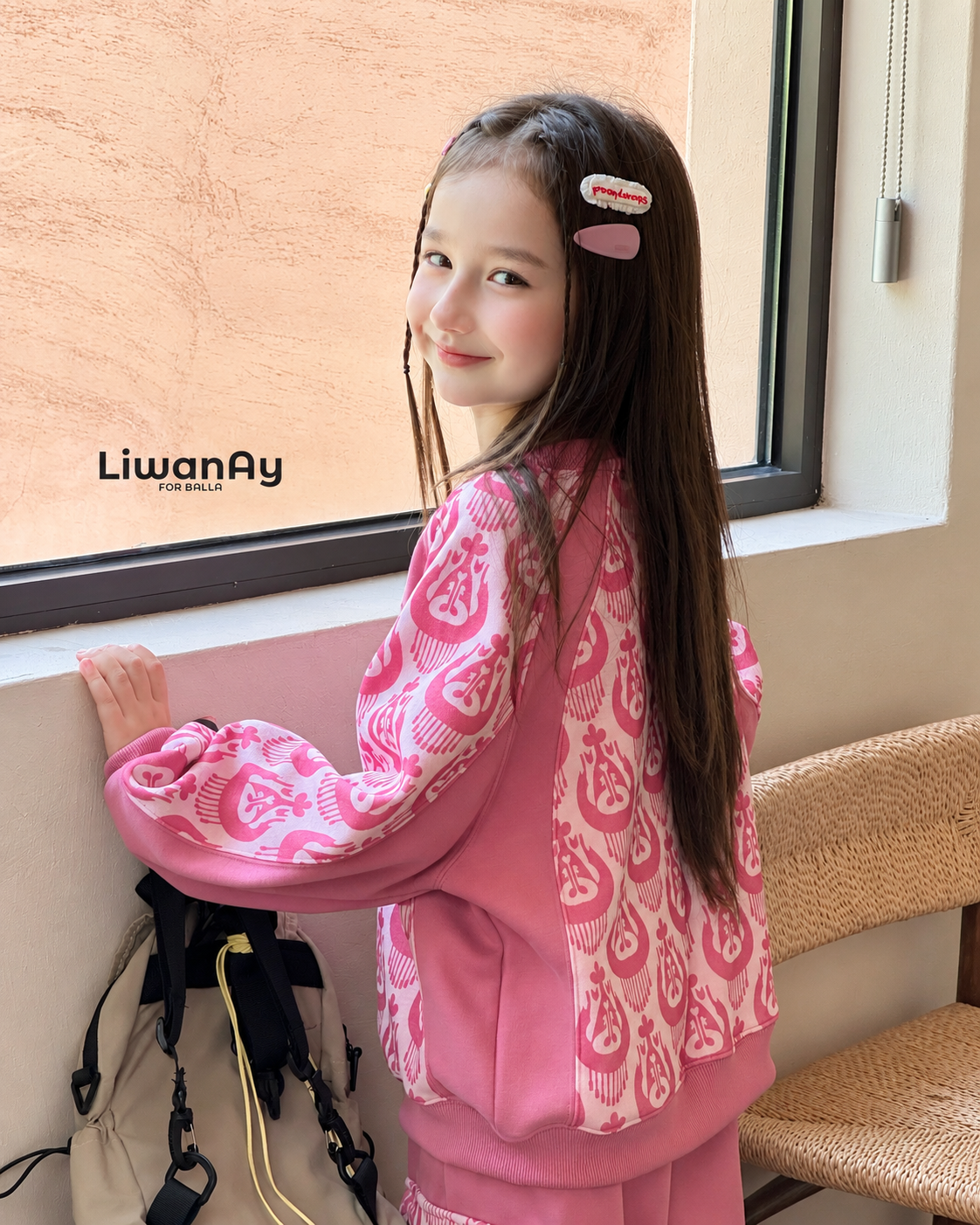 Side view of the girl in the pink ikat set by a window, a backpack hanging nearby.