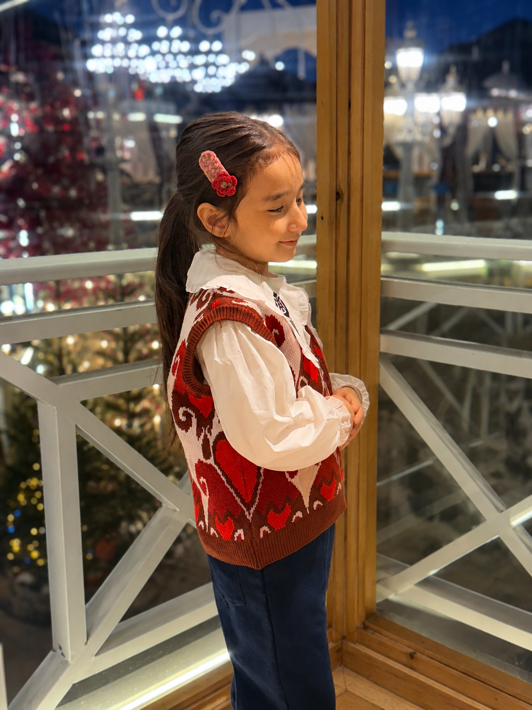 Side view of the girl wearing the red atlas heart knit vest, showing the patterned knit detail on a night terrace