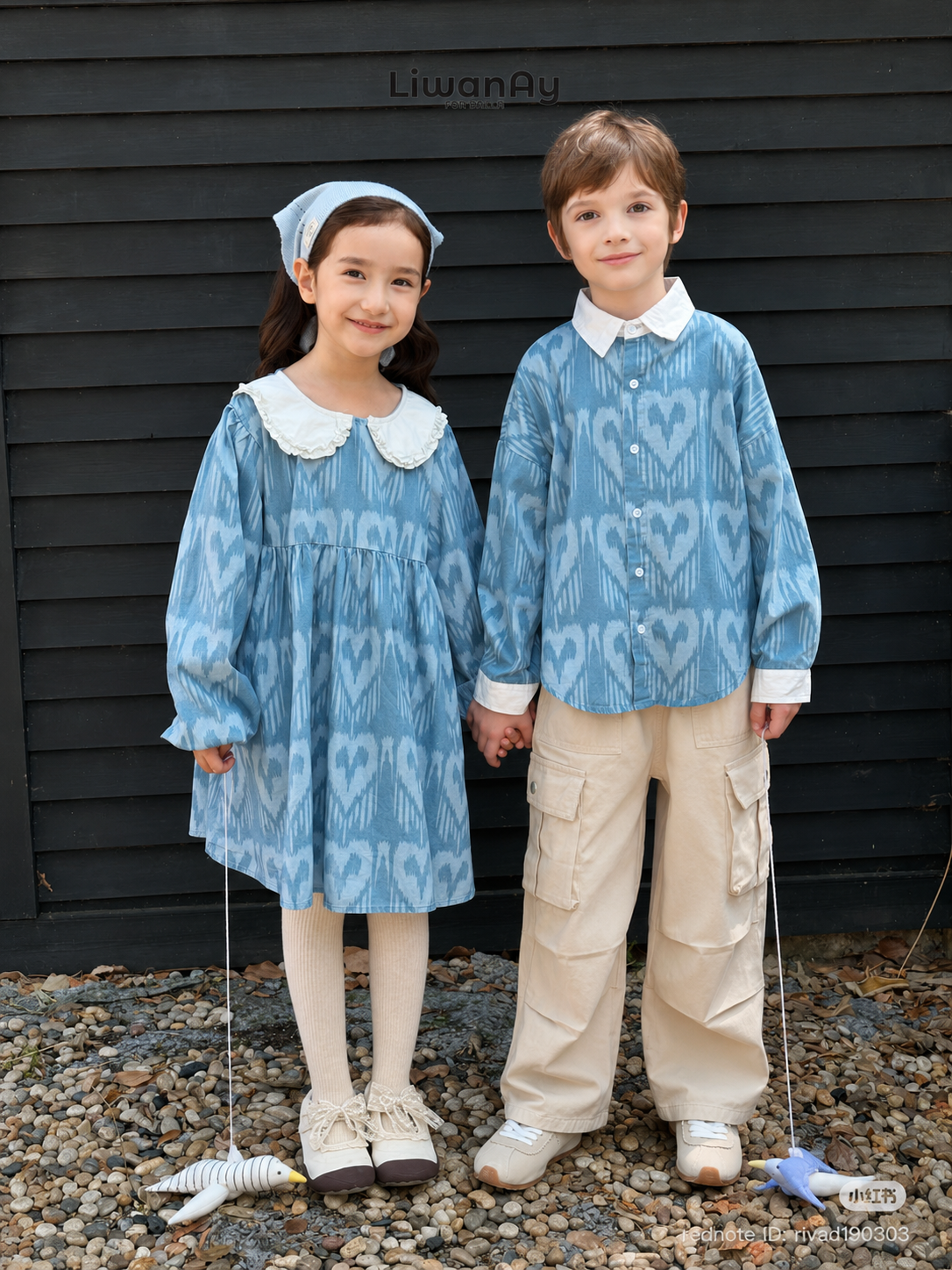 Girl and boy in matching blue ikat outfits with white collars posing together by a dark slatted wall.