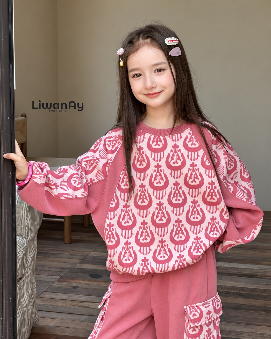 Close-up of the smiling girl in the pink ikat sweatshirt with hair clips, hand on the door.