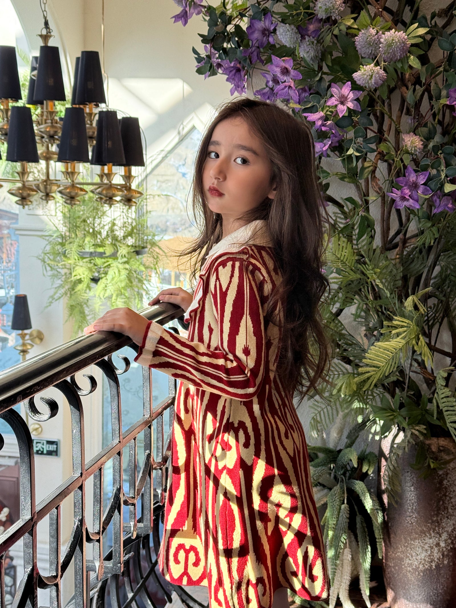 Girl wearing a red Liwanay spring dress with heritage-inspired patterns in a bright indoor garden setting.